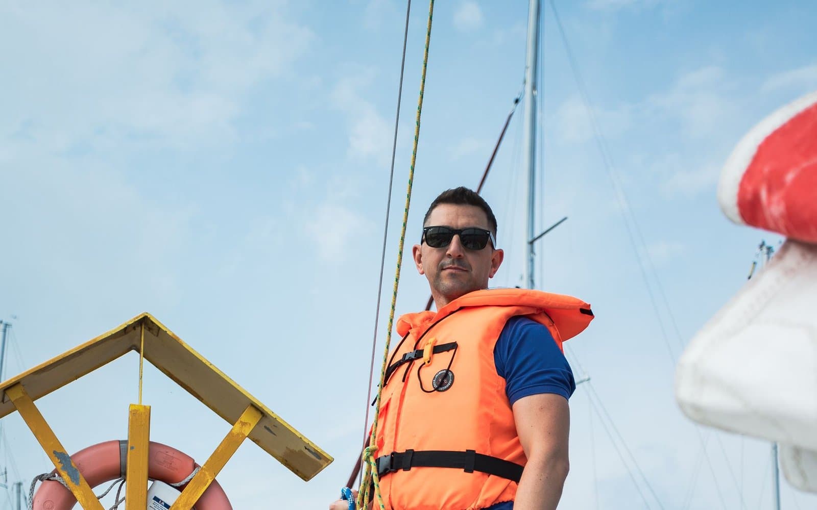Żeglarz w pomarańczowej kamizelce ratunkowej na jachcie w marinie