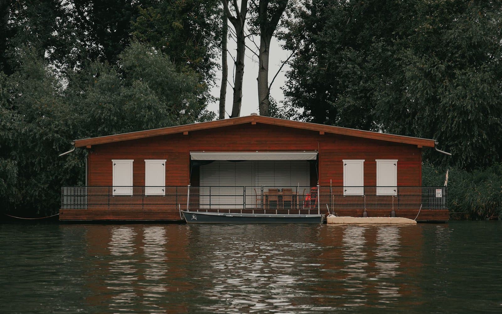 Drewniany houseboat przy zielonym, zalesionym brzegu na spokojnej wodzie